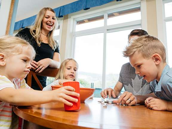 Children playing a game at a wooden table with an adult standing behind them
