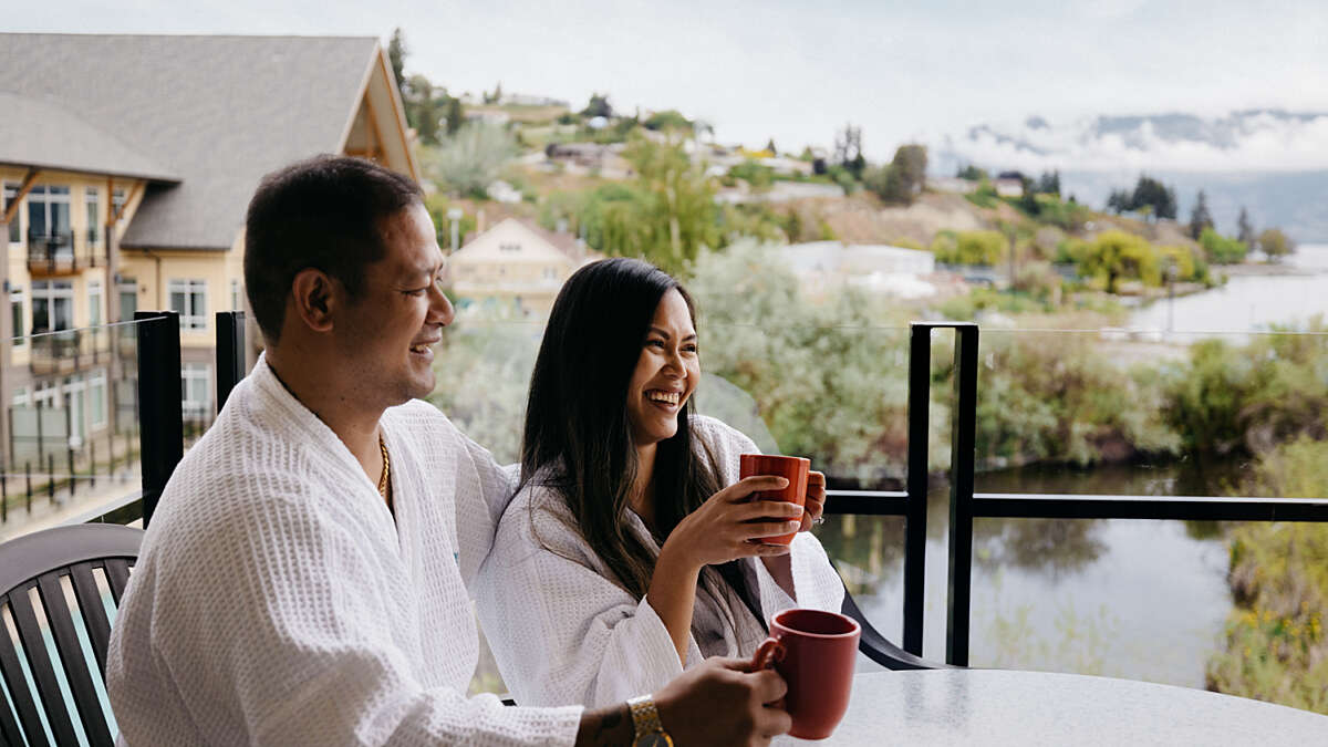 Summerland Waterfront Resort & Spa Gift Certificates - couple smiling and enjoying coffee on the balcony overlooking the lake.