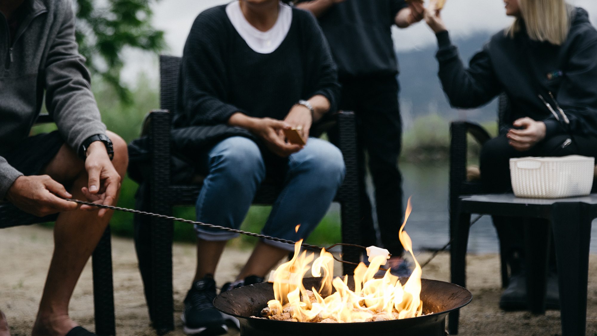 Group of guests gathered around a lakeside fire pit roasting marshmallows at Summerland Waterfront Resort