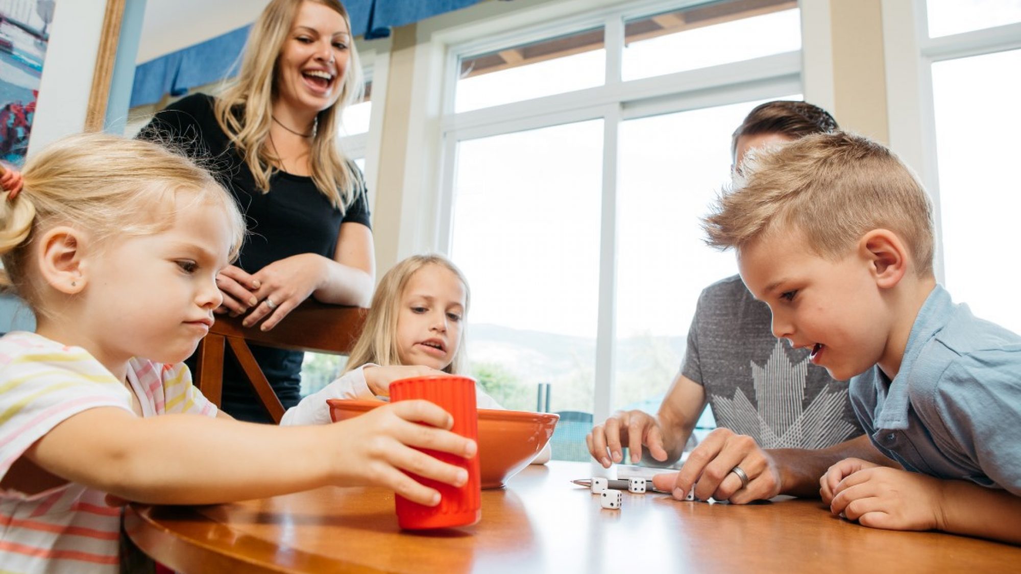 Children playing a game at a wooden table with an adult standing behind them