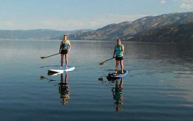 Two women standing on paddleboards on a calm lake with mountains in the background.