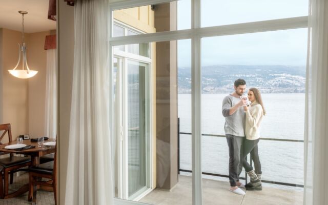 Couple on a lake-view balcony of the hotel suite with dining area visible inside