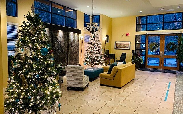 The resort lobby decorated for Christmas, featuring two lit Christmas trees, seating areas, and large windows looking out onto a snowy evening.